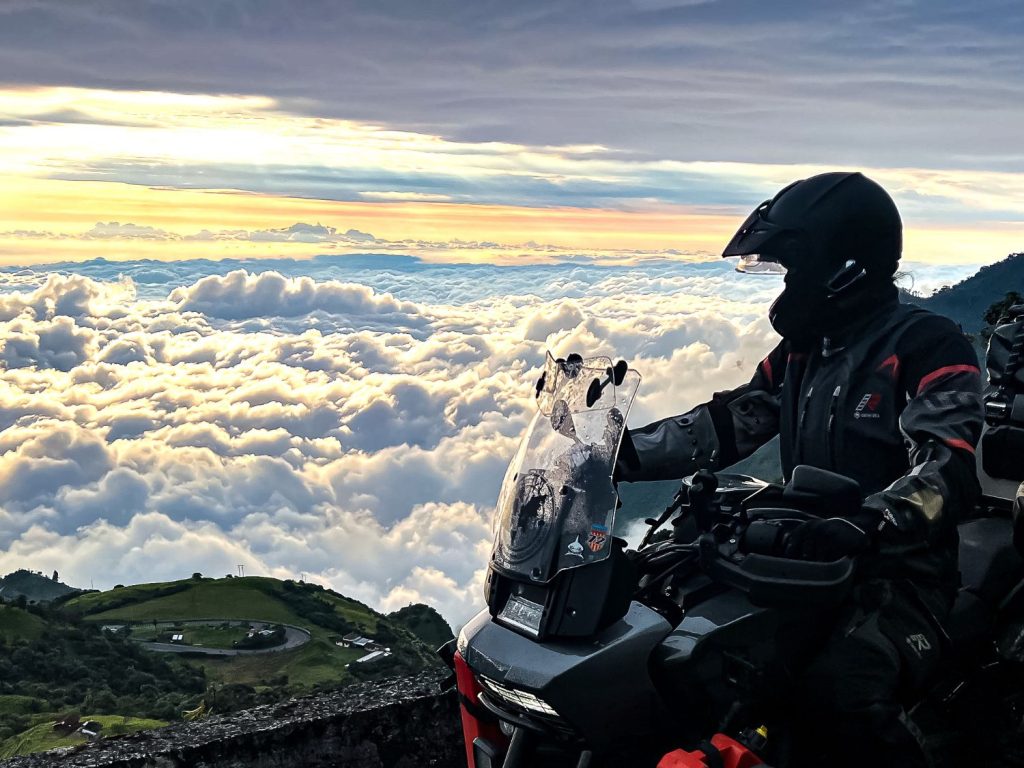 Motorcyclist looking down at clouds and a winding road, high up in Ecuador