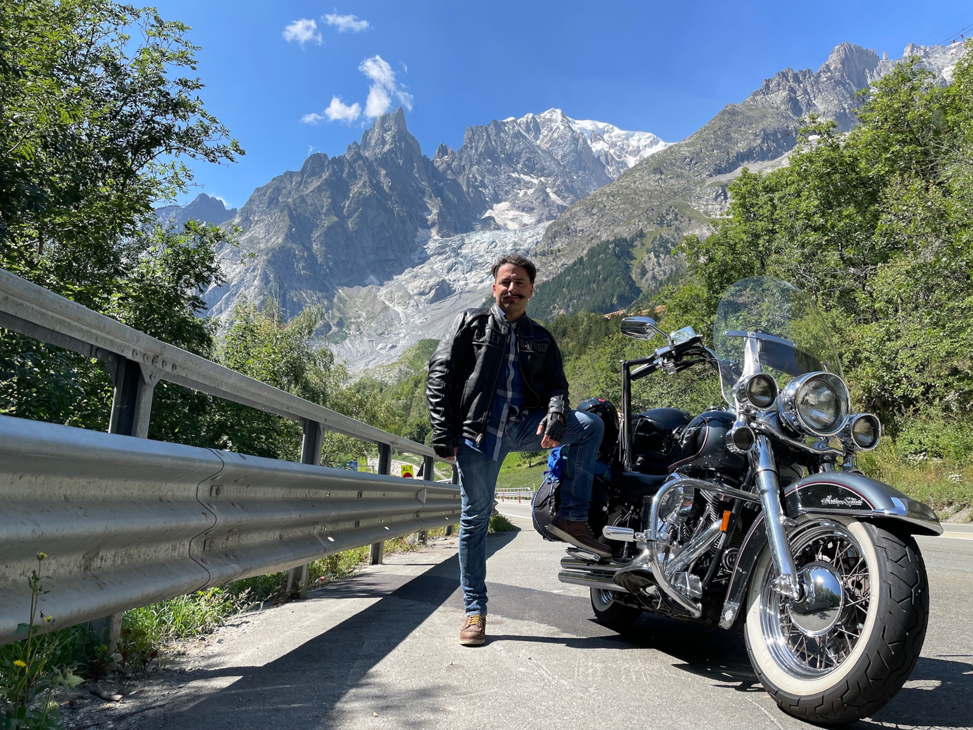 A man standing with his leg resting on a motorbike.