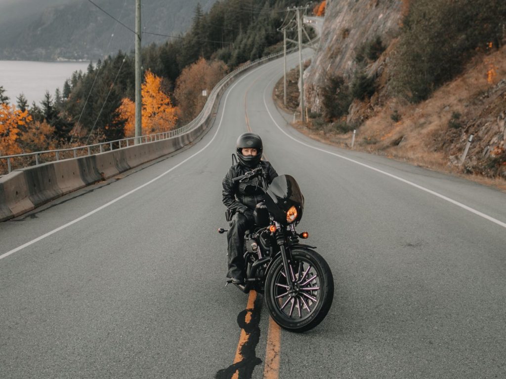 View of ANDRA NEDELCU stationary in the middle of a twisting road on her motorcycle.