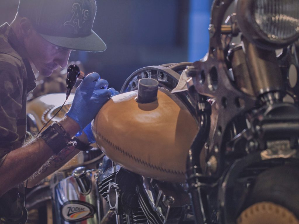 A tattooist works on the leather covering of a Harley-Davidson.