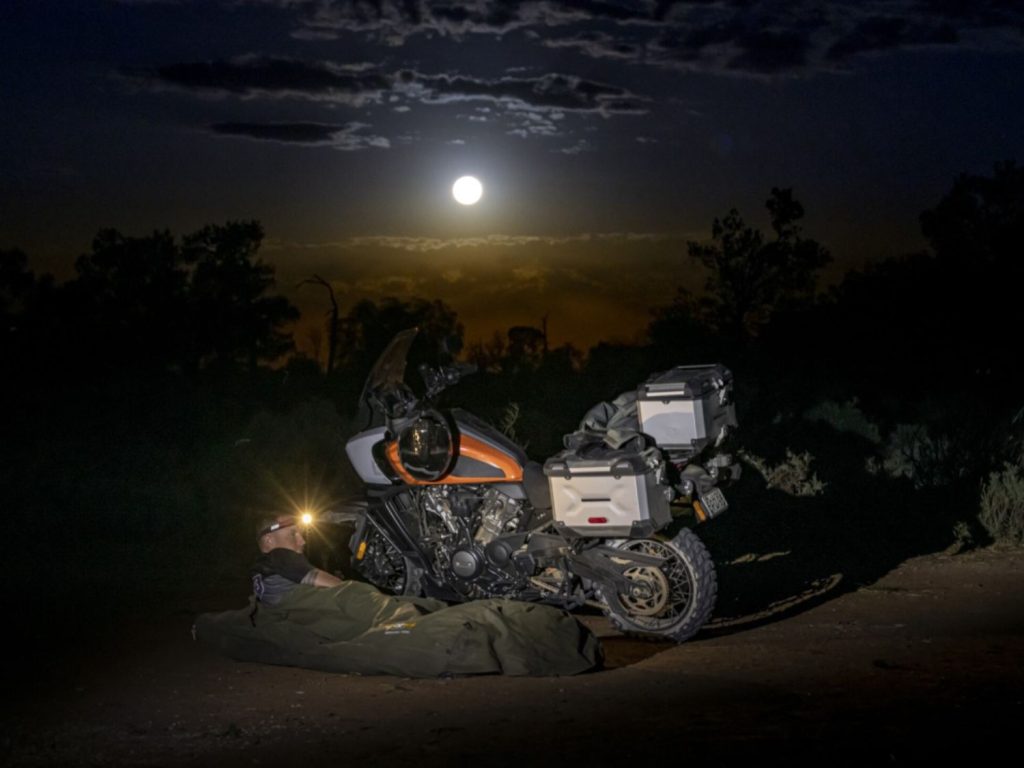 A motorcyclist rests in his sleeping bag next to his motorcycle in the darkness of an Australian night