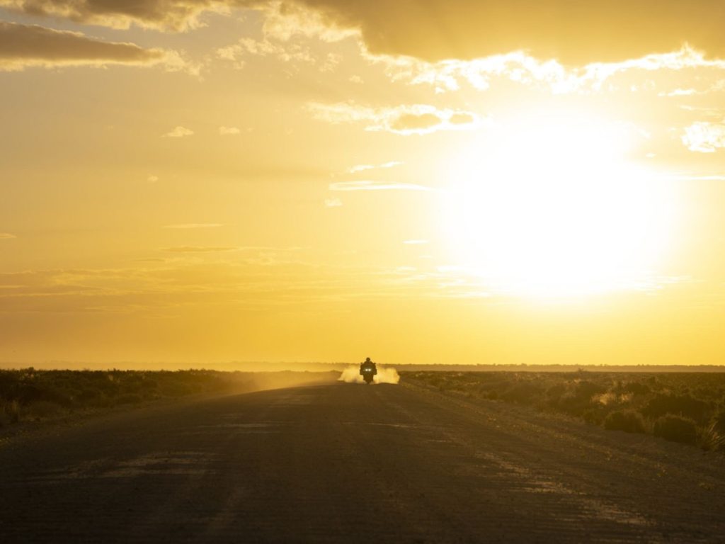 A motorcyclist heads off into the sunset in the Australian wilderness.