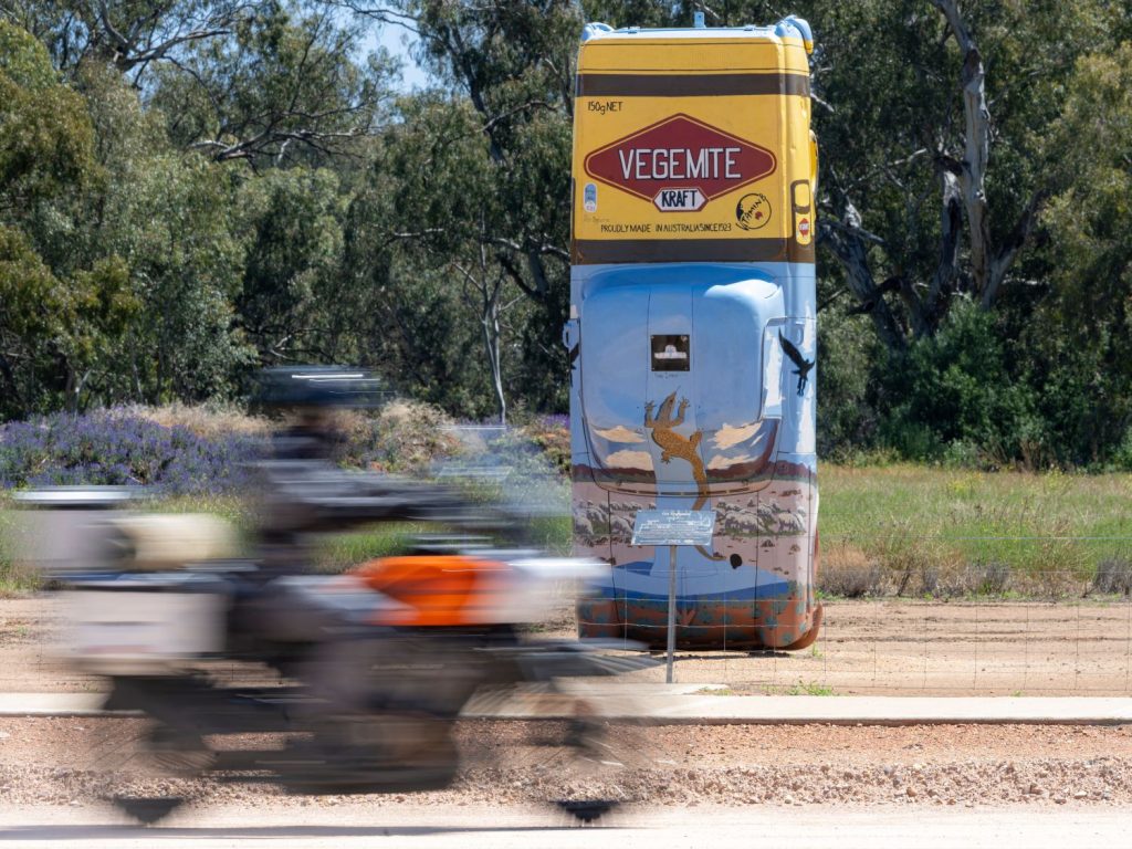 A motorcyclist rides past an advert for vegemite.